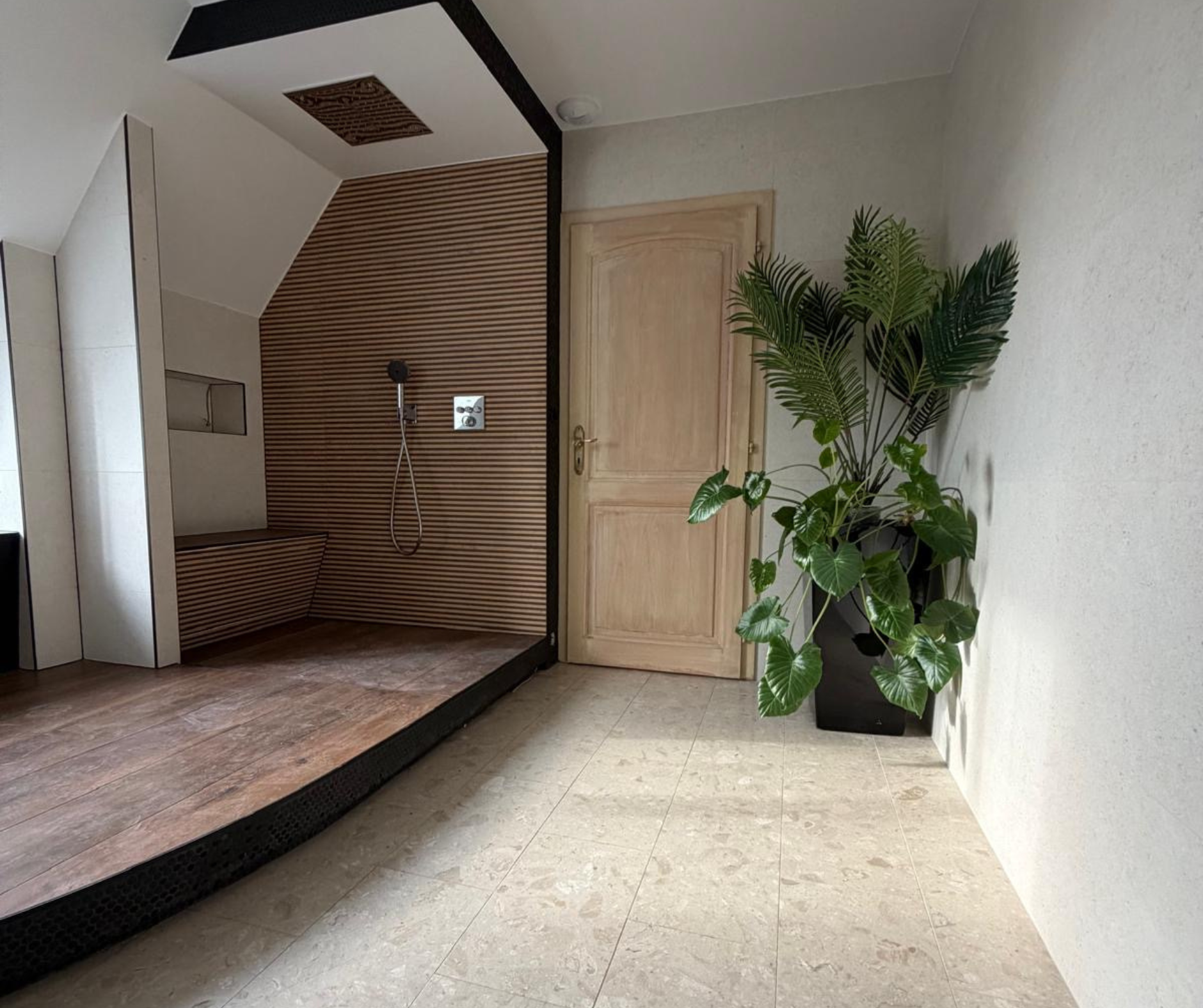 Vue d'ensemble d'une salle de bain spacieuse sous combles avec plateforme en bois, carrelage en pierre naturelle et baignoire îlot bicolore Le Square, projet de rénovation en Alsace.